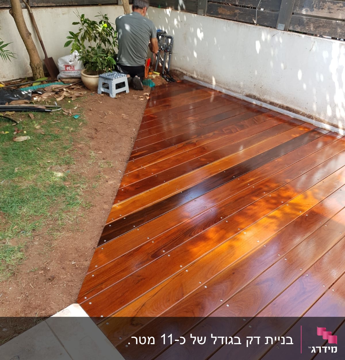 אדם מתקין דק עץ בגינה ליד קיר וגדר.